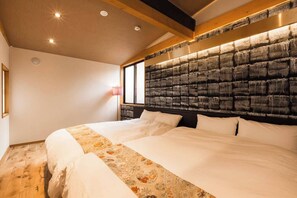 Ein großes Bett mit einem gemusterten Überwurf, ein Kopfteil mit strukturierter Optik und ein Fenster mit Blick nach draußen.