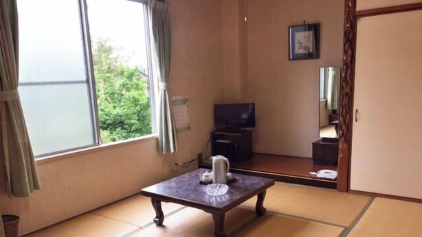 A traditional Japanese room with tatami flooring, a low table with a candle, a television, and a sliding door. - Business Hotel Yamatoya (Iizuka)