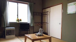 A room with tatami flooring, a futon bed, a table with a kettle, a heater, and a window with curtains. - Business Hotel Yamatoya (Iizuka)
