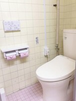 Un baño con inodoro, repisa con toallas rosas y panel de control en la pared.