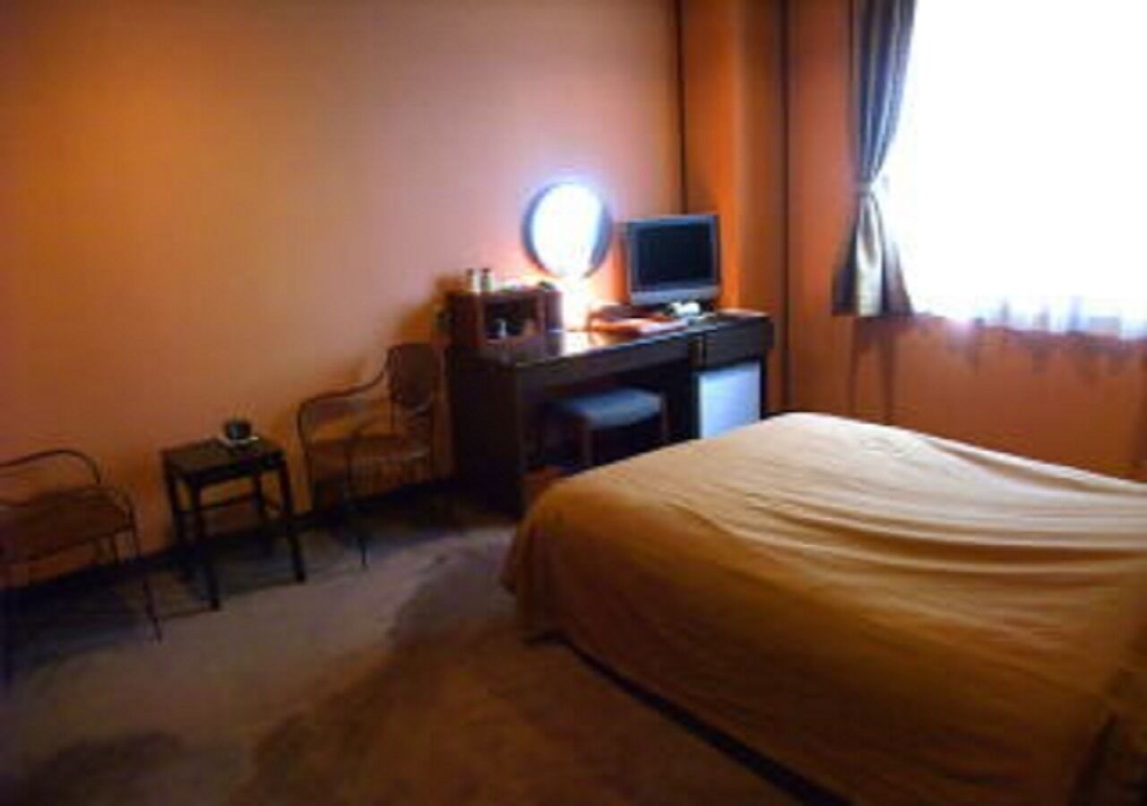 Una habitación de hotel con una cama, un escritorio con una computadora, una silla y una mesita.
