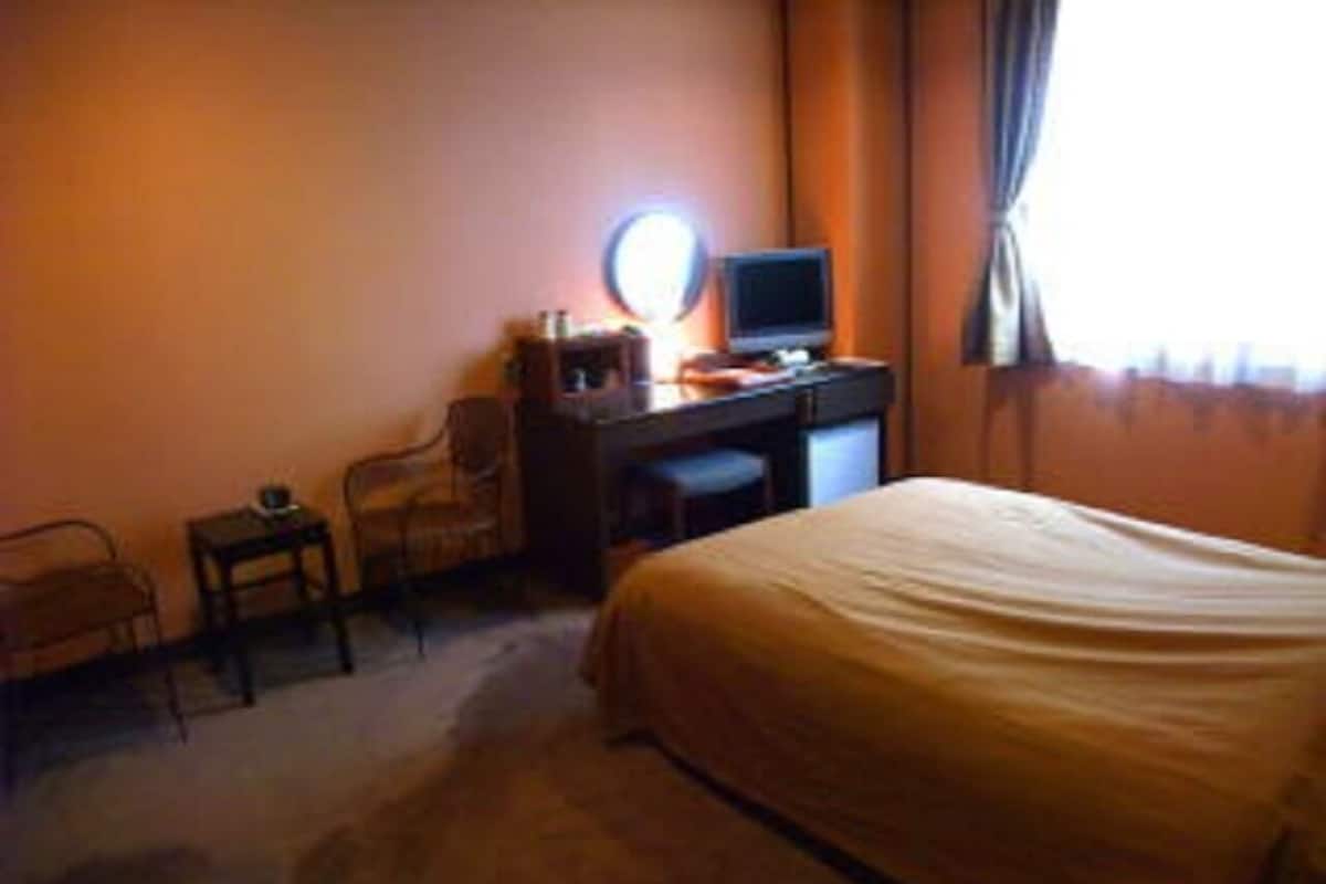 A hotel room with a bed, a desk with a computer, a chair, and a small table.