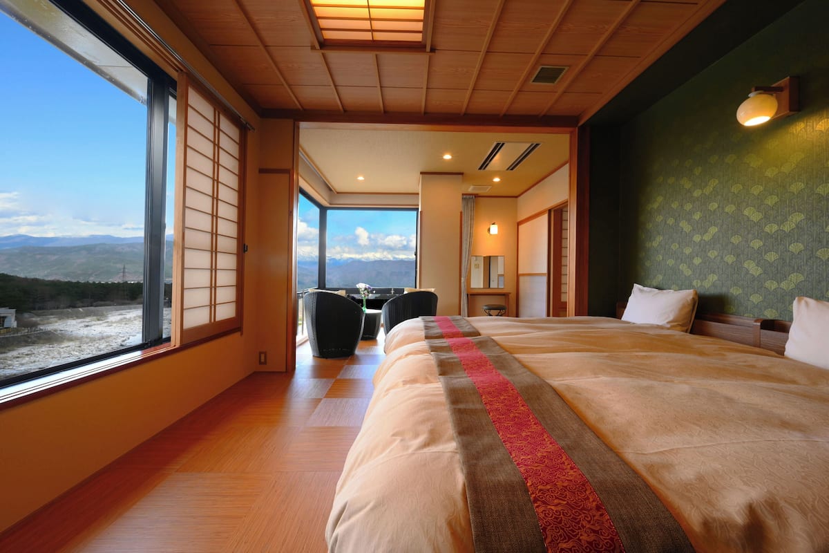 A hotel room with a large bed, a view of the mountains, and a dining area with chairs.