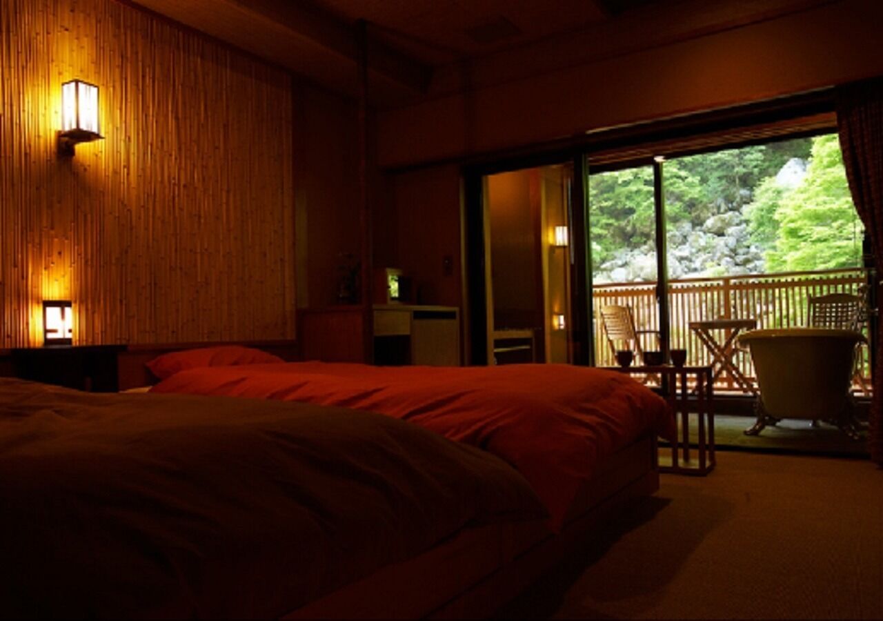 Un dormitorio con una cama grande, una pared de madera y una puerta corredera que da a un espacio exterior con una silla y una bañera.
