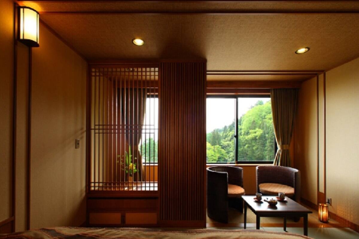 A traditional Japanese room with tatami flooring, a low table with a cushion, a chair, and a window with a view of greenery.
