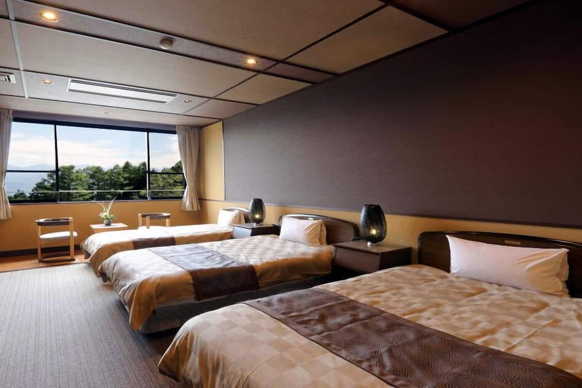 A hotel room with two beds, a large window with a view, a small table, and a nightstand with a lamp.