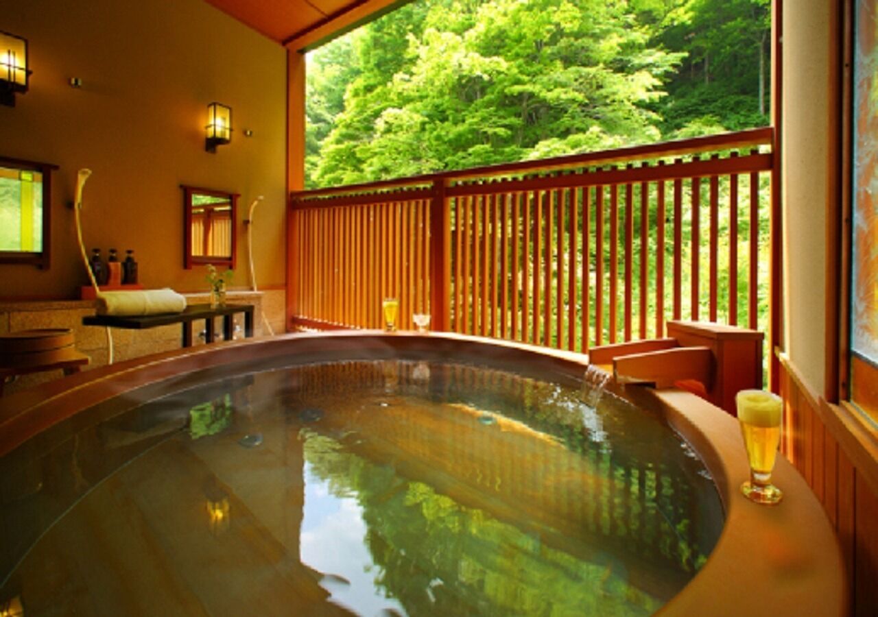 Un jacuzzi con cubierta de madera, una cerveza y vistas a un bosque.