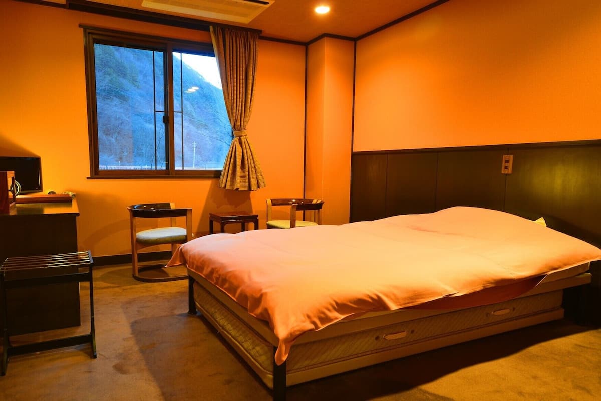 A hotel room with a bed, two chairs, a desk, and a window with curtains.