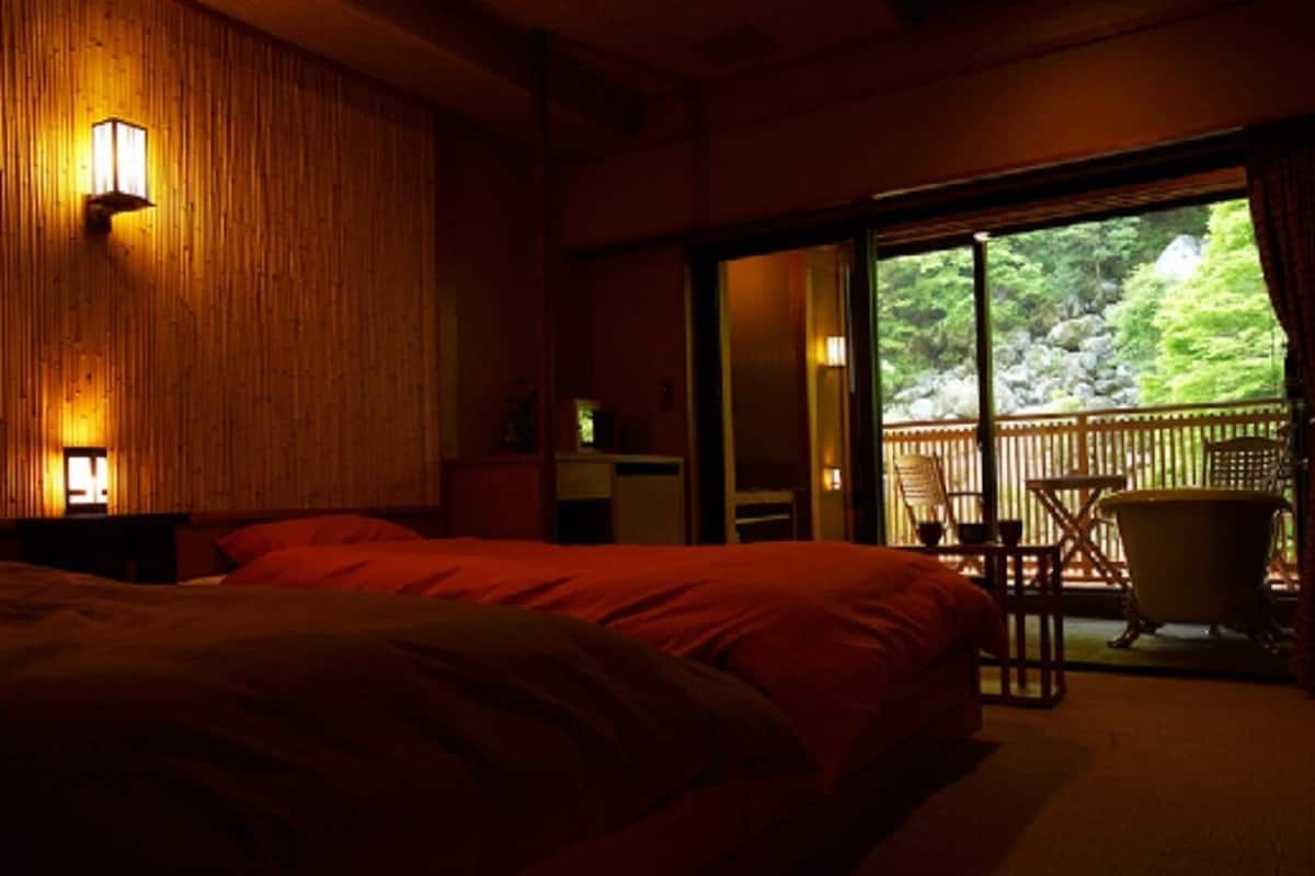 A bedroom with a large bed, a wooden wall, and a sliding door leading to an outdoor area with a chair and a bathtub.