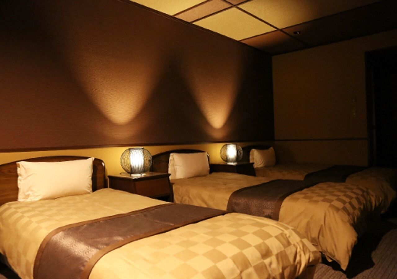 Una habitación de hotel con tres camas, cada una con cabecero, mesitas de noche y lámparas.