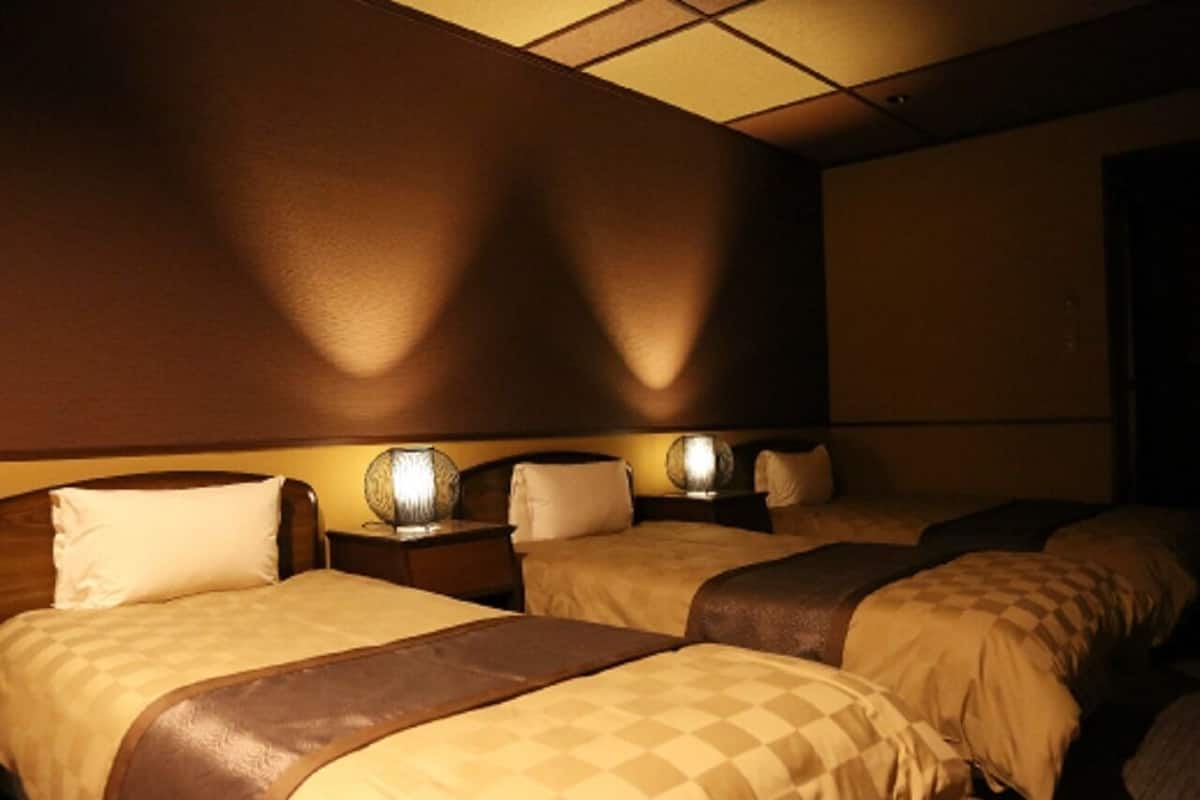 A hotel room with three beds, each with a headboard, bedside tables, and lamps.