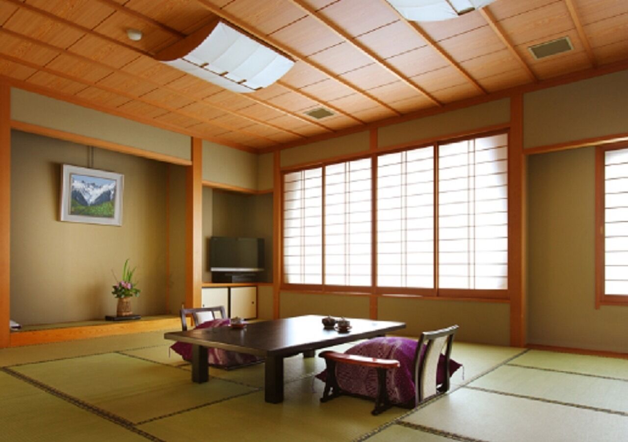 Una habitación tradicional japonesa con suelo de tatami, una mesa baja, un televisor y puertas correderas.