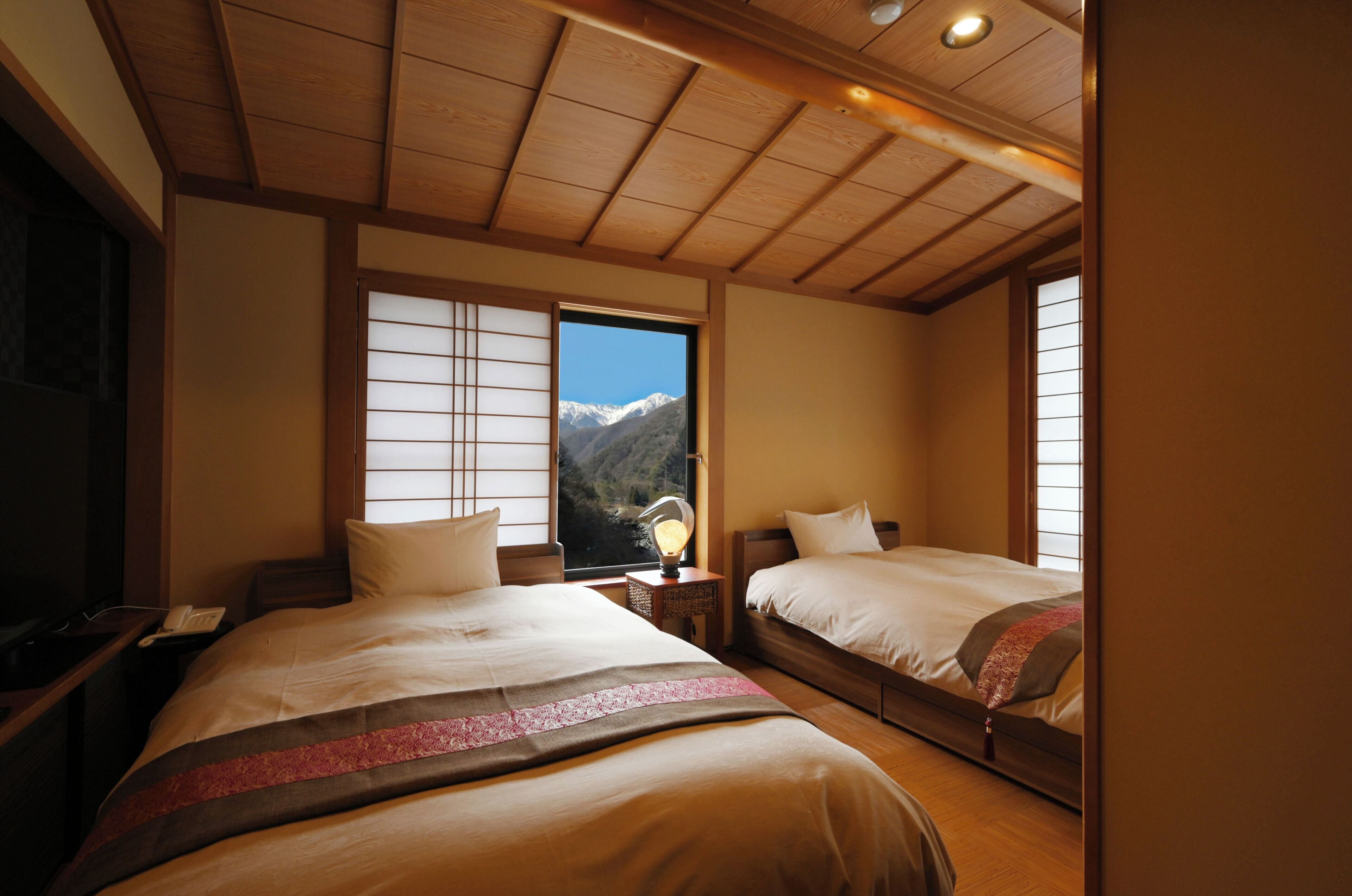 Habitación de hotel con dos camas, techo de madera y ventana con vistas a la montaña.