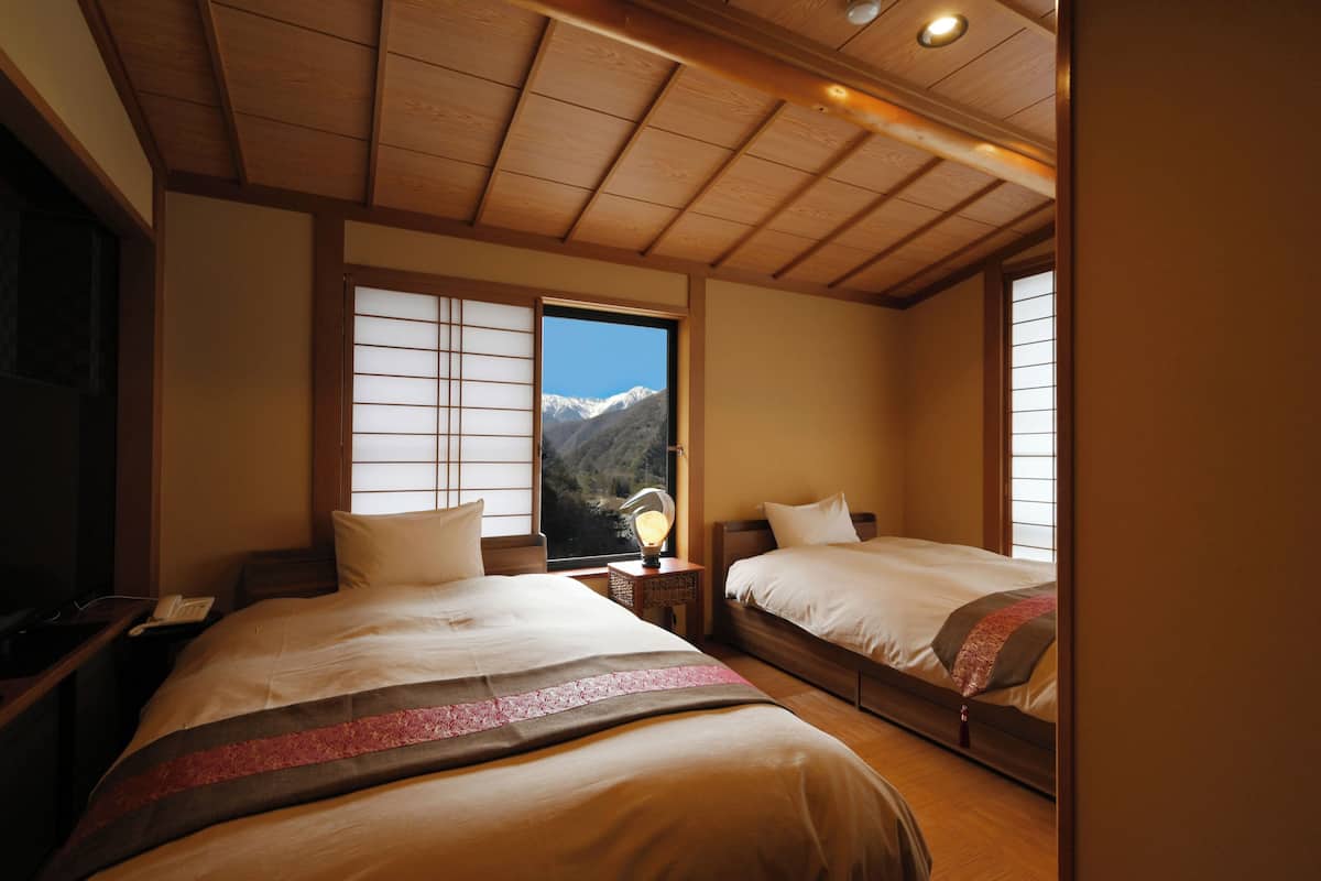 A hotel room with two beds, wooden ceiling, and a window with a mountain view.