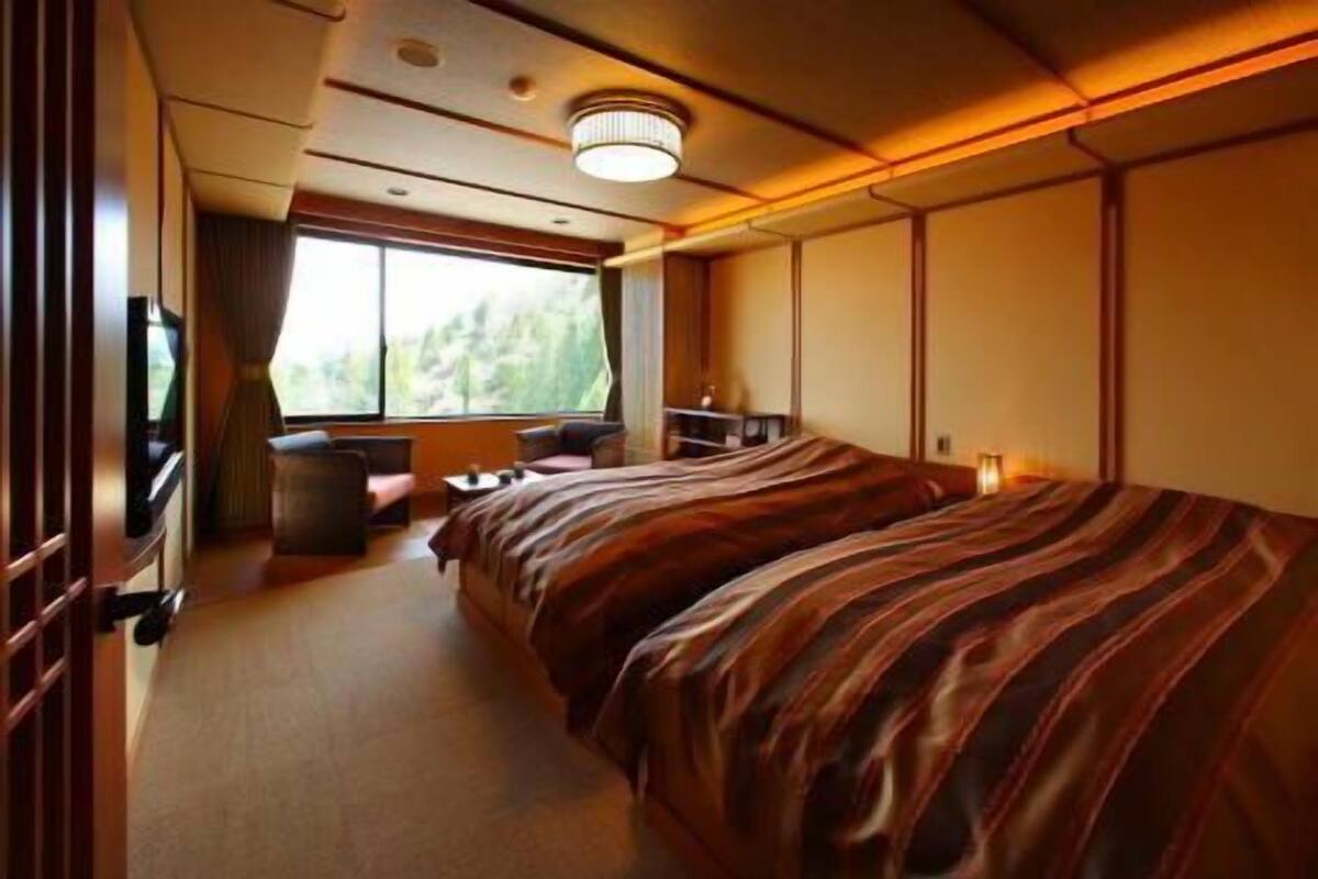A room with a bed, a small table, a chair, a TV, and a window.