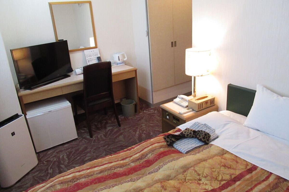 A hotel room with a bed, desk, chair, television, lamp, and a small refrigerator.