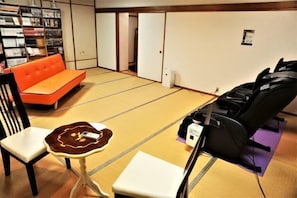 A tatami mat room with a sofa, chairs, a small table, and massage chairs. - New Royal Hotel (Omuta)