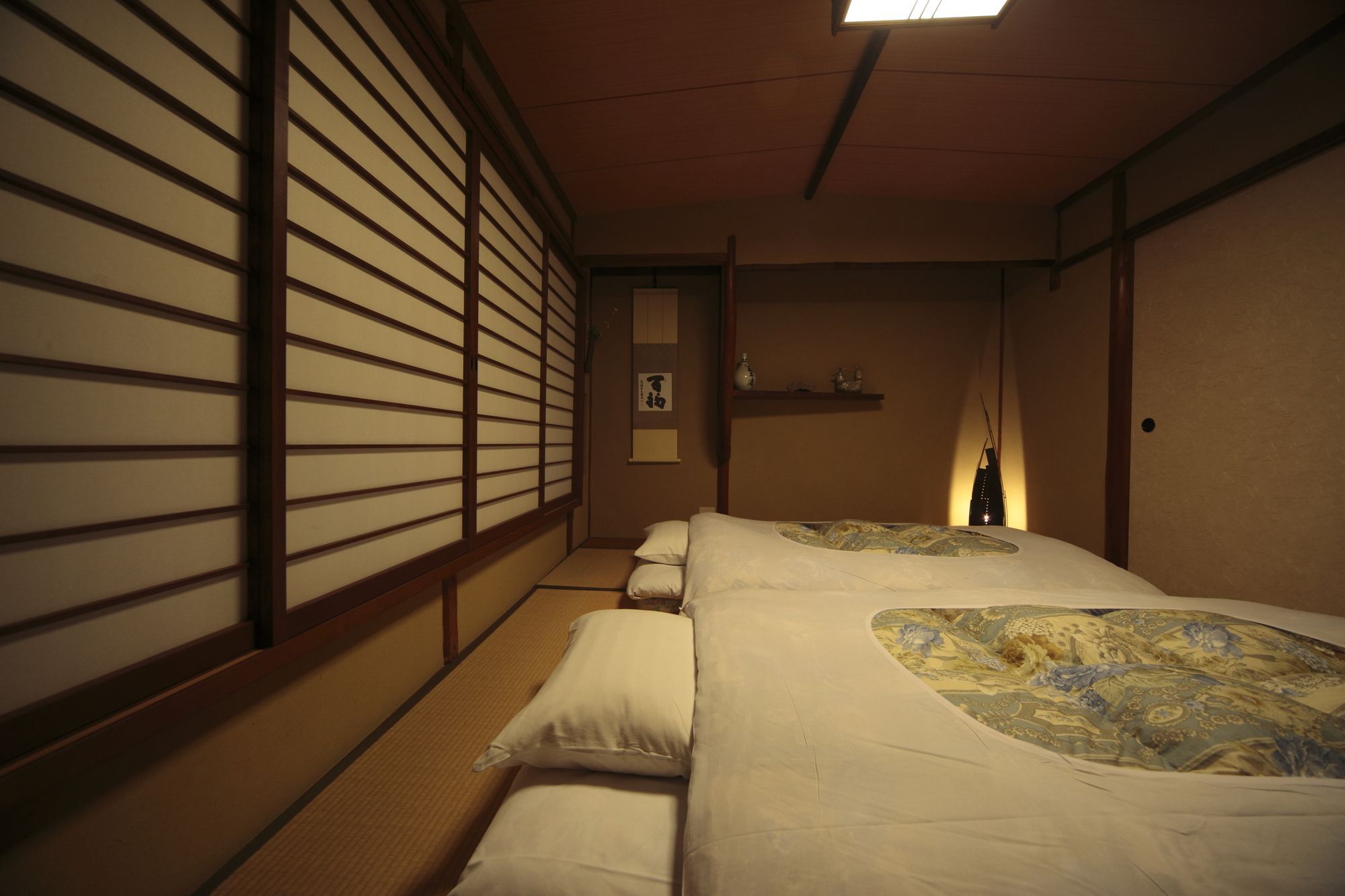 Una habitación tradicional japonesa con suelo de tatami, una cama baja con colcha estampada y paneles shoji en las paredes.
