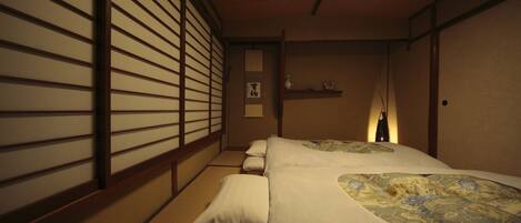 A traditional Japanese-style room with tatami flooring, a low bed with a patterned bedspread, and shoji screens on the walls.