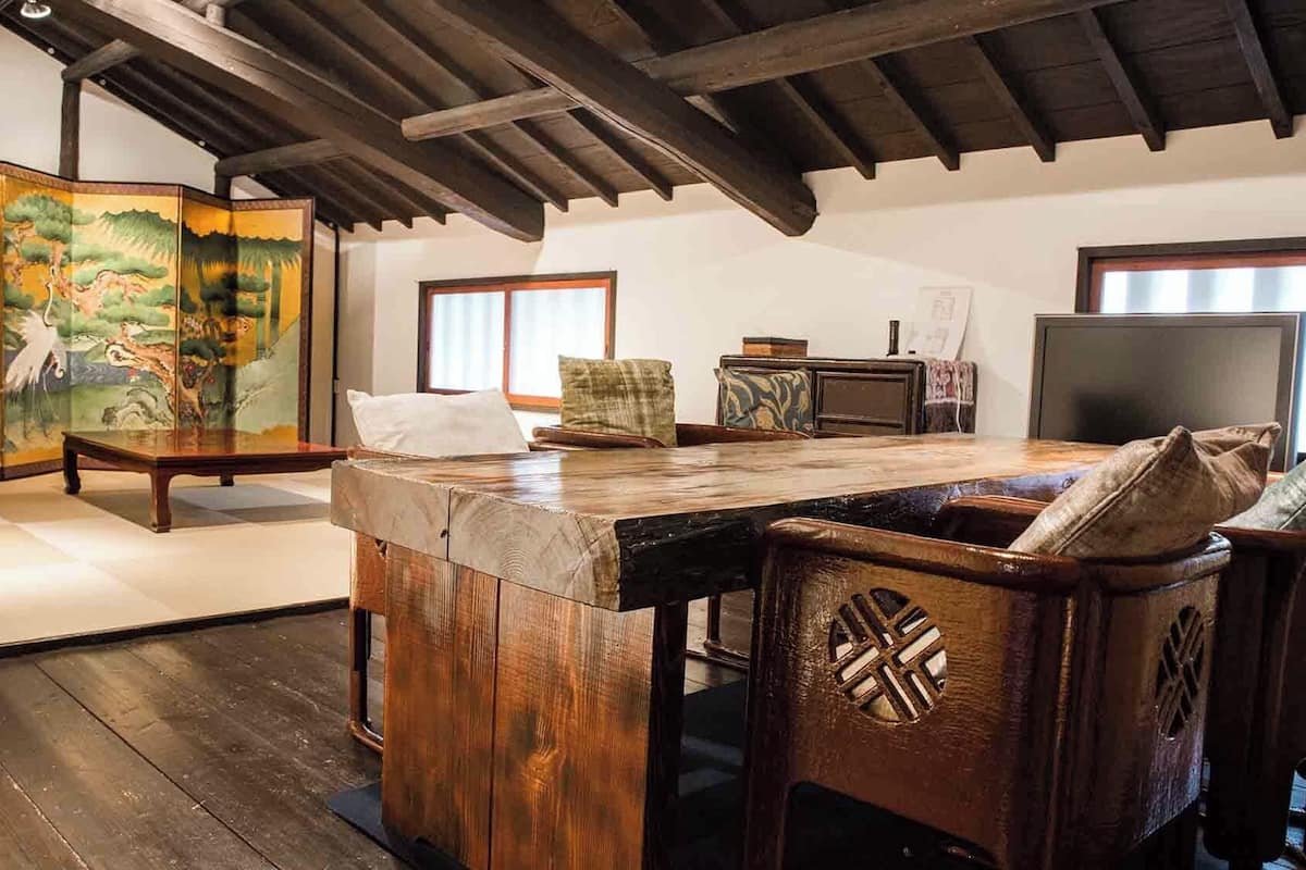 Ein traditioneller japanischer Raum mit Tatami-Böden, einem niedrigen Holztisch, einem Holzschrank, einem Fernseher und einem Shoji-Bildschirm mit Landschaftsbild.