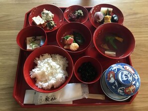 En traditionell japansk bento-låda med ris, olika grönsaker och en dekorativ keramikskål.