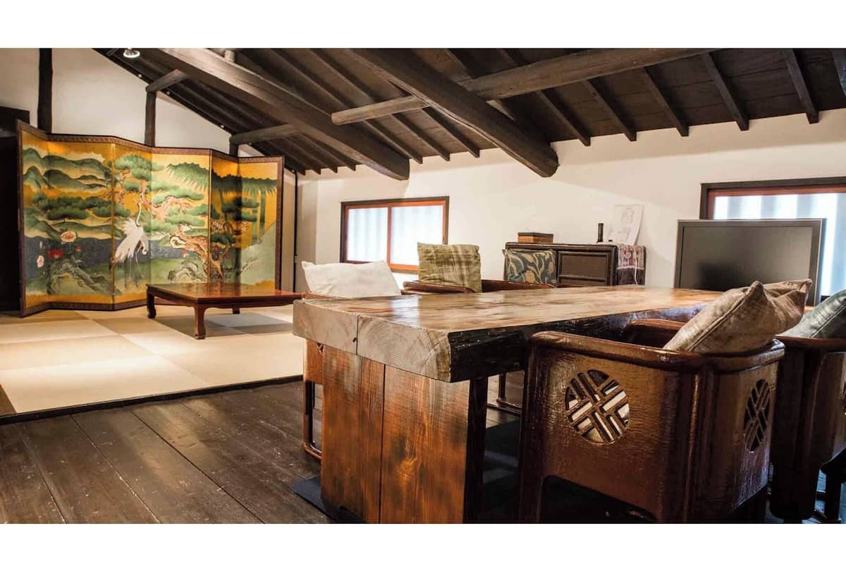 Ein traditioneller japanischer Raum mit Tatami-Böden, einem niedrigen Holztisch und einem großen Shoji-Bildschirm mit Landschaftsmalerei.