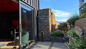 Un bâtiment moderne doté d’une façade en pierre, d’une entrée avec une porte en verre et d’un espace jardin agrémenté de plantes et d’une statue.