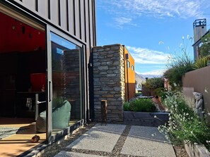 A modern building with a stone facade, a glass door entrance, and a garden area with plants and a statue. - Modern Wanaka Escape with Mezzanine Loft (Wānaka)