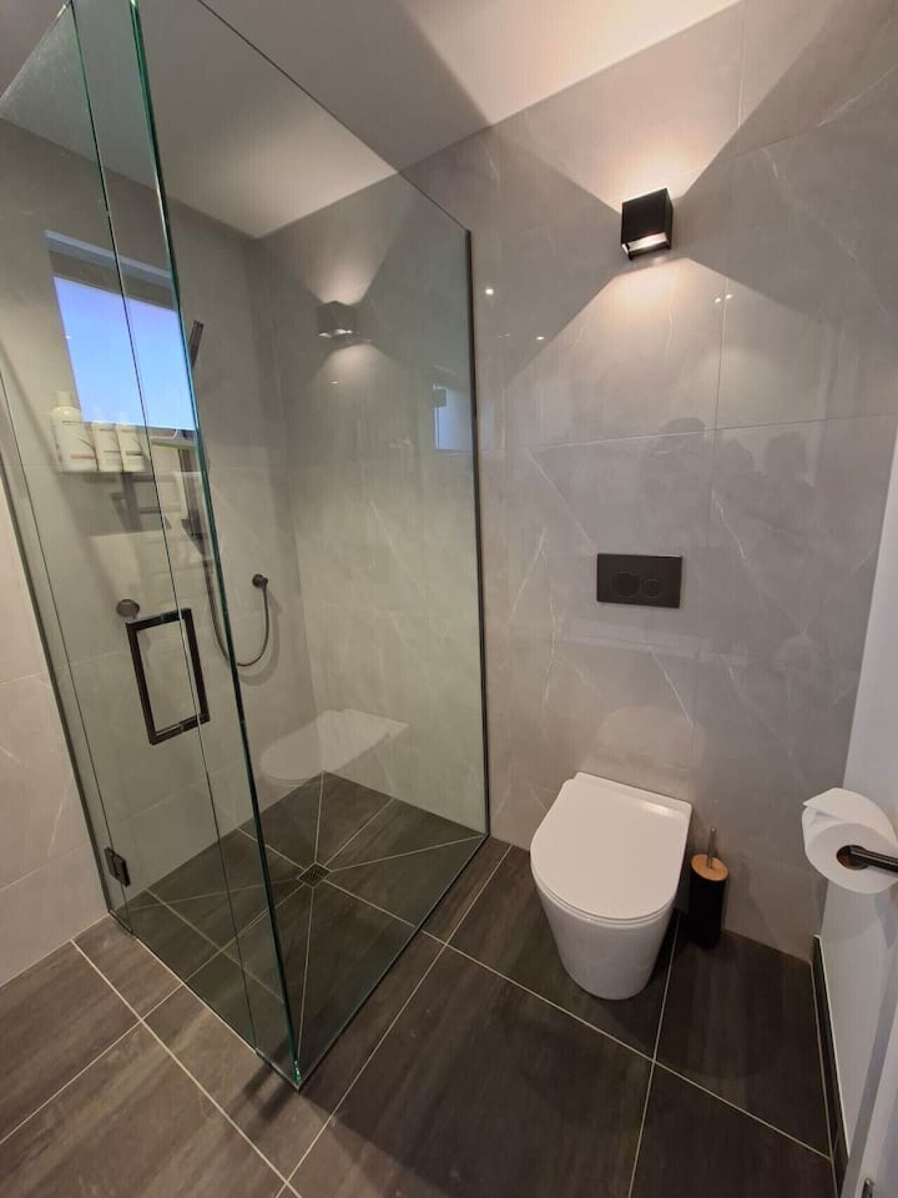 Un baño moderno con cabina de ducha de vidrio, inodoro y un portalámparas instalado en la pared.