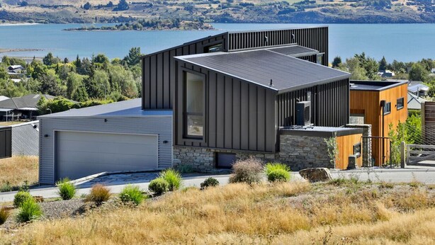 Une maison moderne avec un garage, des fondations en pierre et une vue sur un lac.