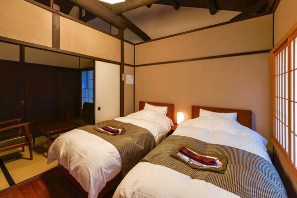Habitación de hotel tradicional japonesa con dos camas, vigas de madera, suelo de tatami y una puerta corredera.