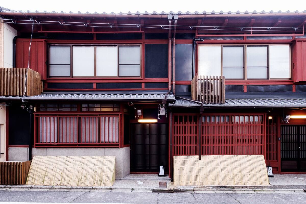 Un edificio japonés tradicional con varias puertas correderas de madera, un tejado de tejas y una pequeña estructura de madera a la izquierda.