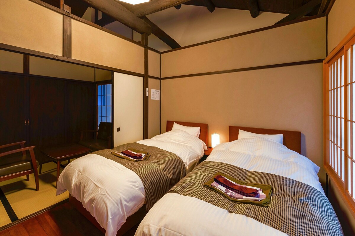 Ein Hotelzimmer mit zwei Betten, einer Holzbalkendecke und Blick durch ein Fenster.