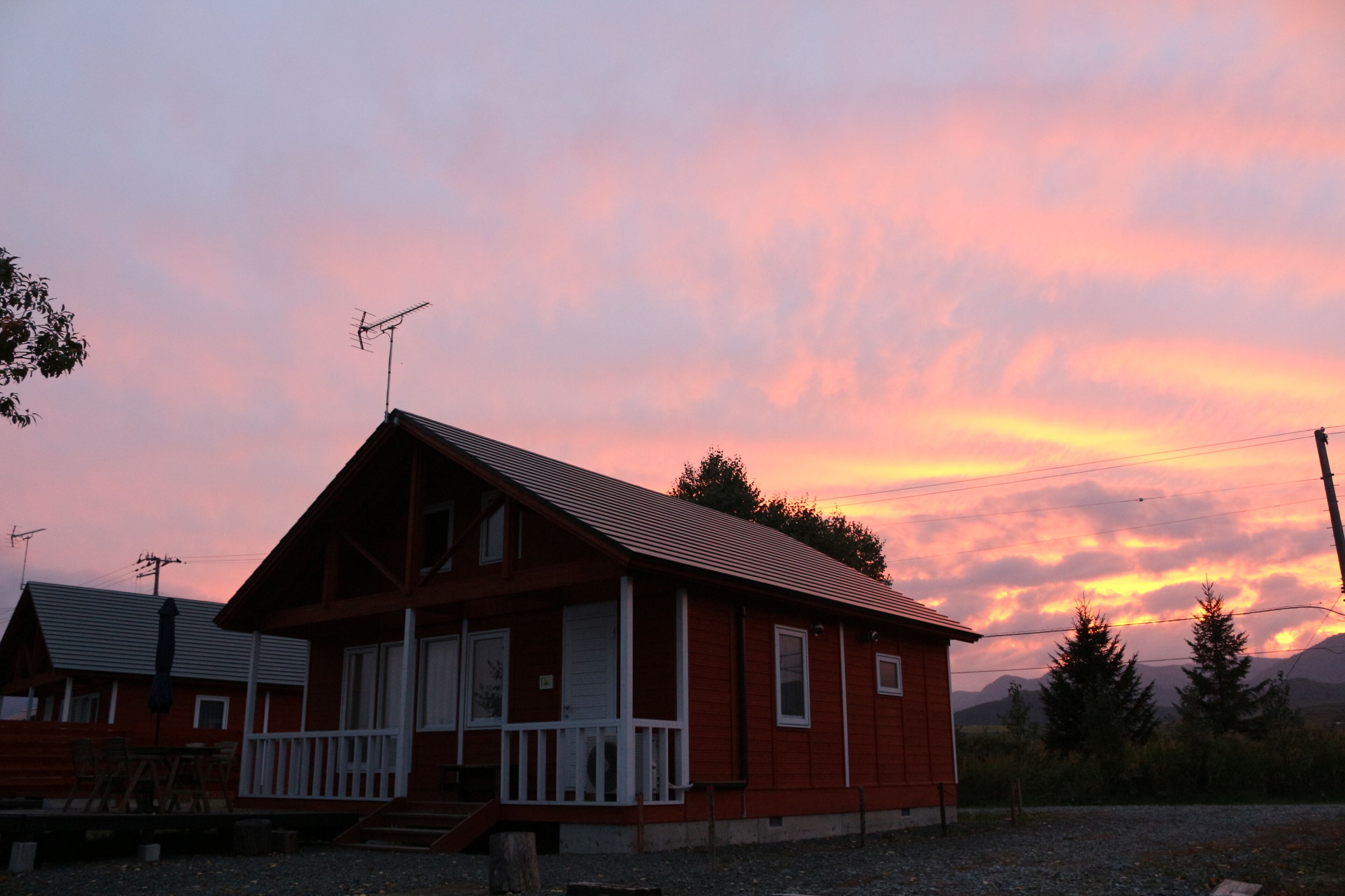 A red cabin with a white porch, a chimney, and a satellite dish.