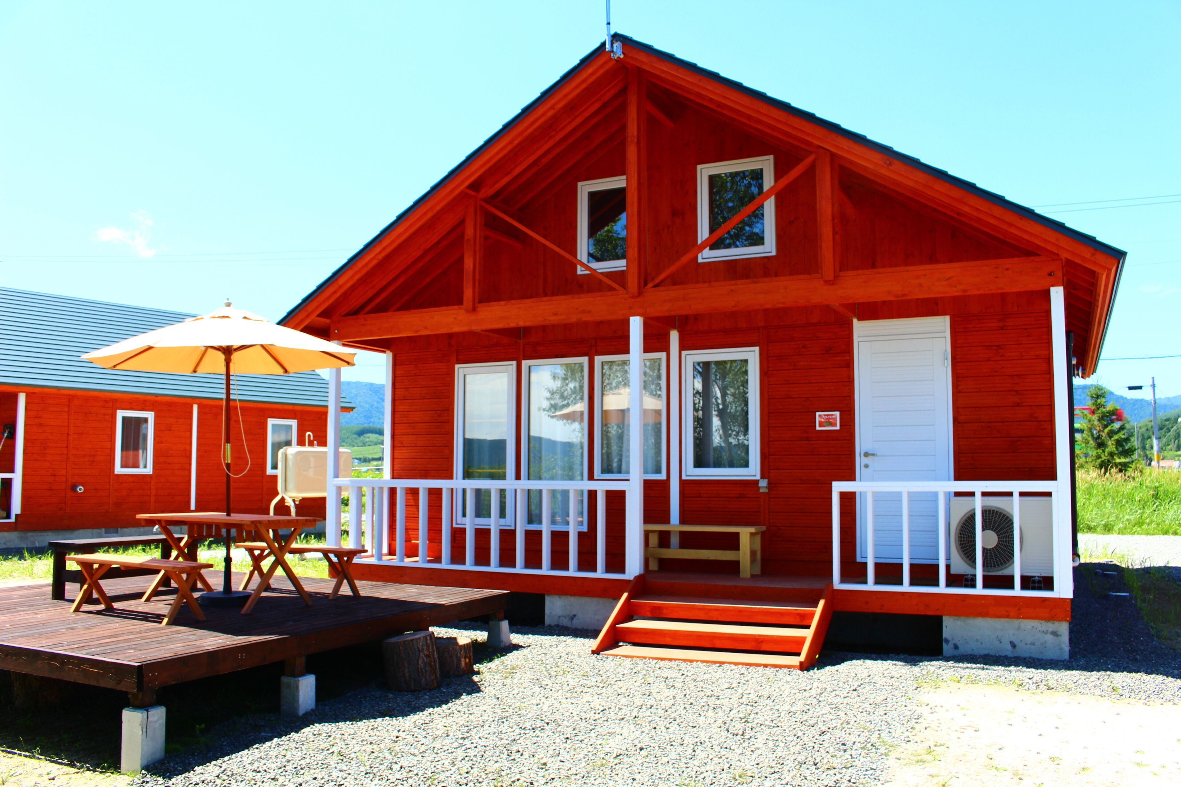 A red wooden cabin with a porch, a picnic table, and an umbrella.