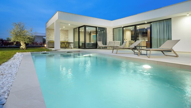 Una casa moderna con piscina, sillas de descanso y un patio con paredes de cristal.