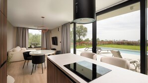Una cocina moderna con una isla central, comedor con sillas y vista a una piscina.