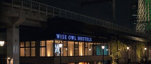 Een gebouw met een bord waarop 'WISE OWL HOSTELS' staat, 's nachts.