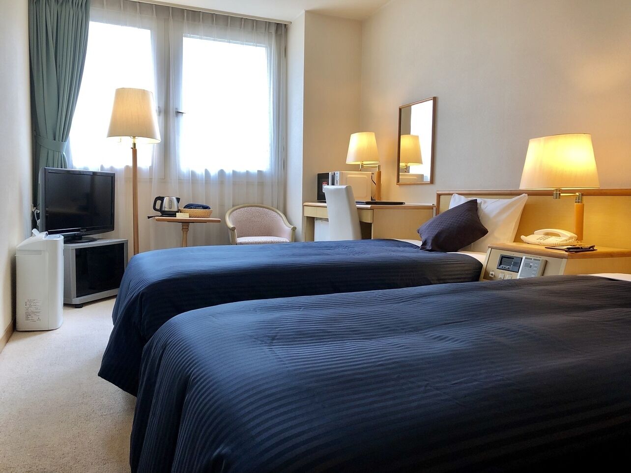 A hotel room with two beds, a TV, a desk with a lamp, a chair, and a bedside table with a phone.