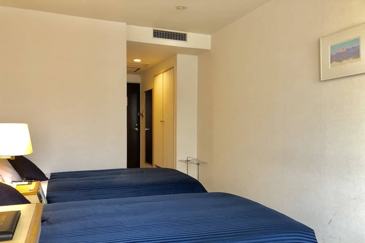 A hotel room with two beds, a desk with a lamp, and a framed picture on the wall.