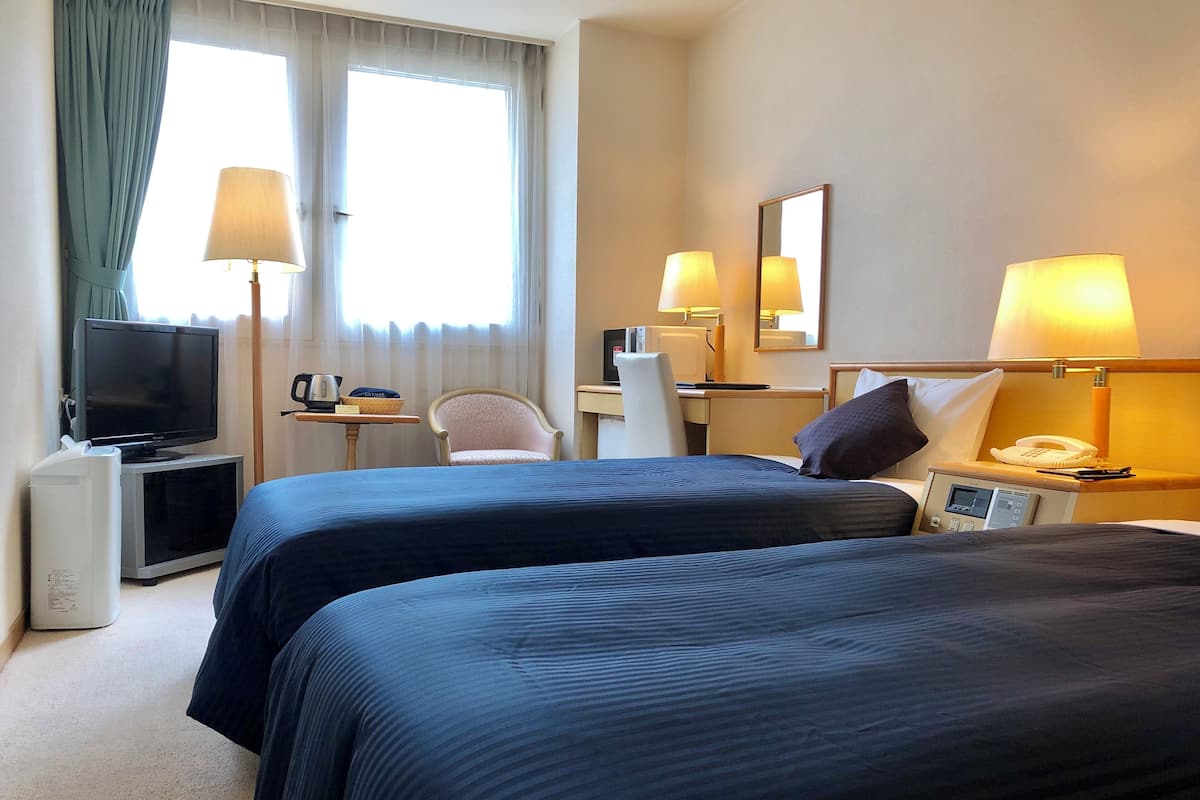 A hotel room with two beds, a desk with a computer, a television, and a chair.