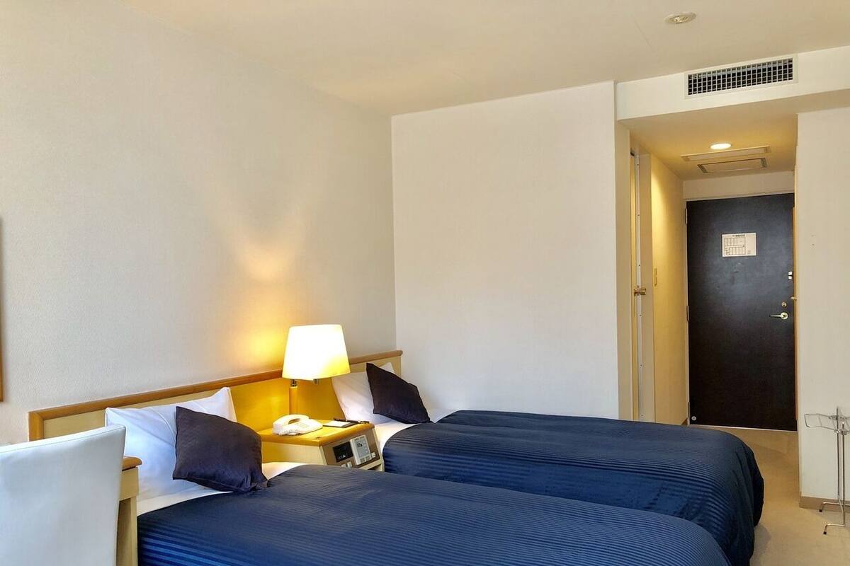 A hotel room with two beds, a nightstand with a lamp, a phone, and a door with a lock.