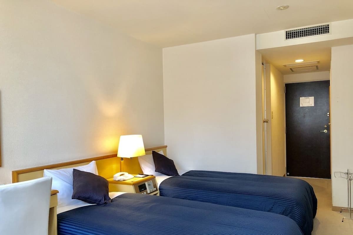 A hotel room with two beds, a nightstand with a lamp, a phone, and a door with a lock.