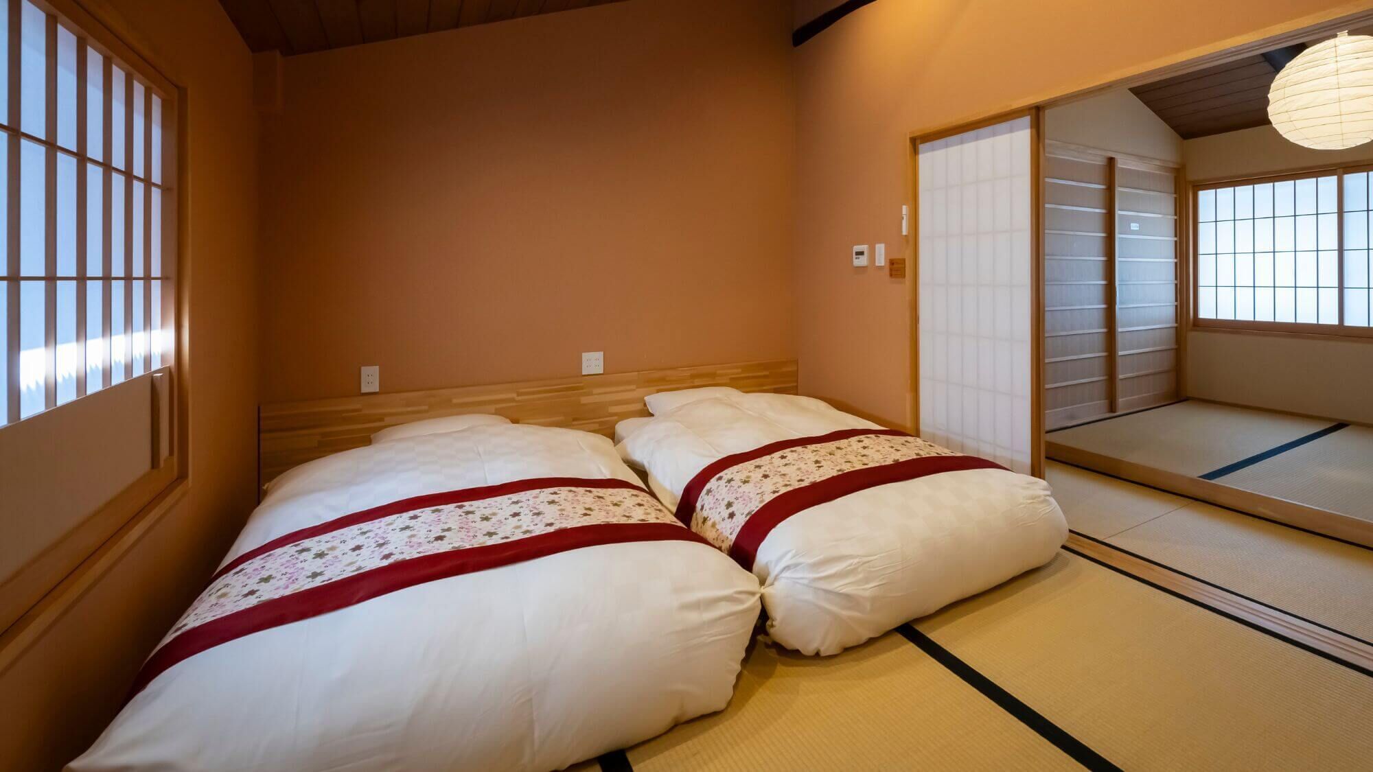 Ein traditioneller japanischer Raum mit Tatami-Bodenbelag, einem niedrigen hölzernen Bett mit weißer Bettwäsche und gleitenden Shoji-Schiebetüren.