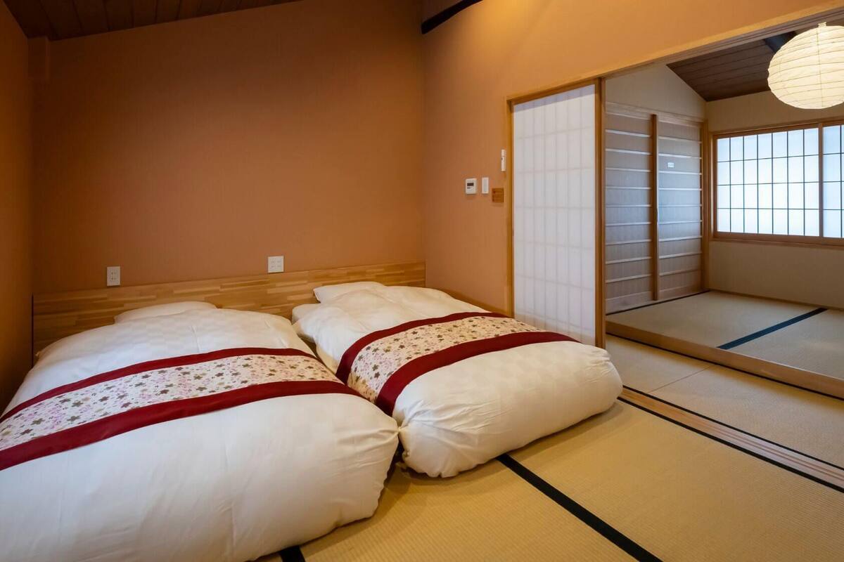 A traditional Japanese room with tatami flooring, a low wooden bed with white bedding, and sliding shoji doors.