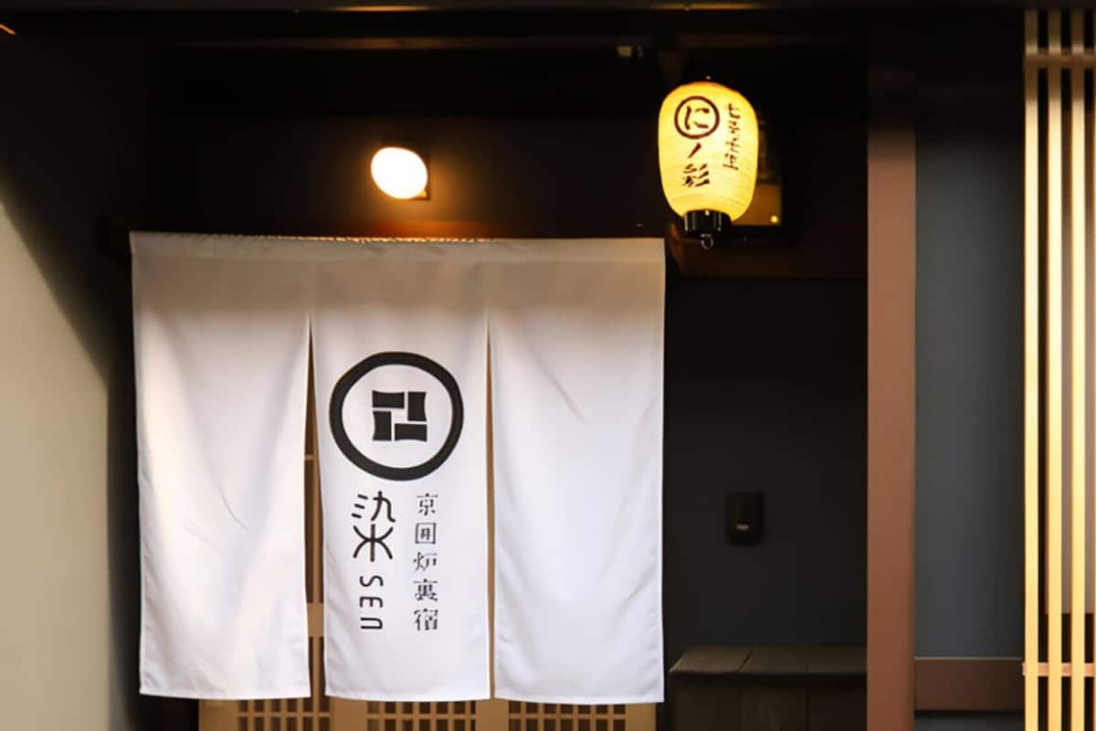 A room with a white curtain displaying a logo and Japanese text, a traditional Japanese lantern, and a sliding door.