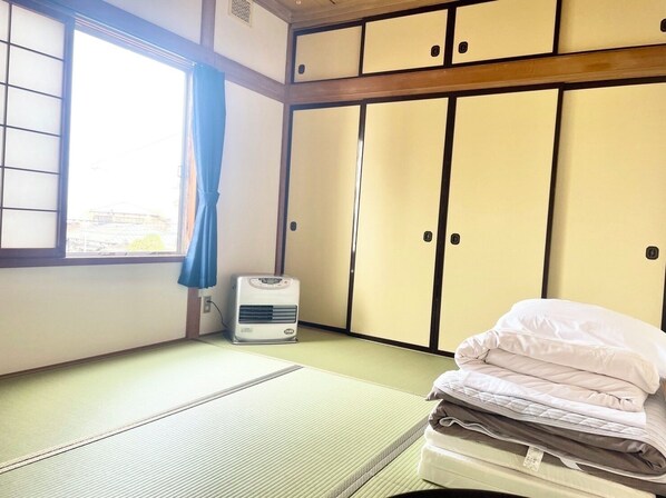 A room with tatami flooring, a bed with pillows, a heater, and sliding doors. - Tsubaki House (Hakodate)