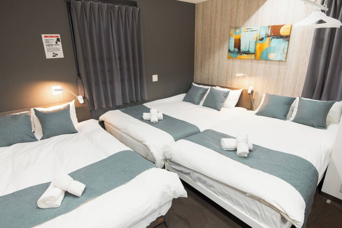 Une chambre d’hôtel avec trois lits, chacun agrémenté de draps blancs et turquoise, et un tableau accroché au mur.