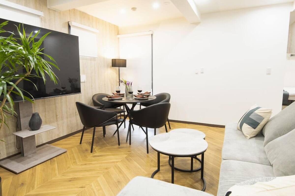 A modern living room with a flat-screen TV, a dining table with chairs, a sofa, and a potted plant.