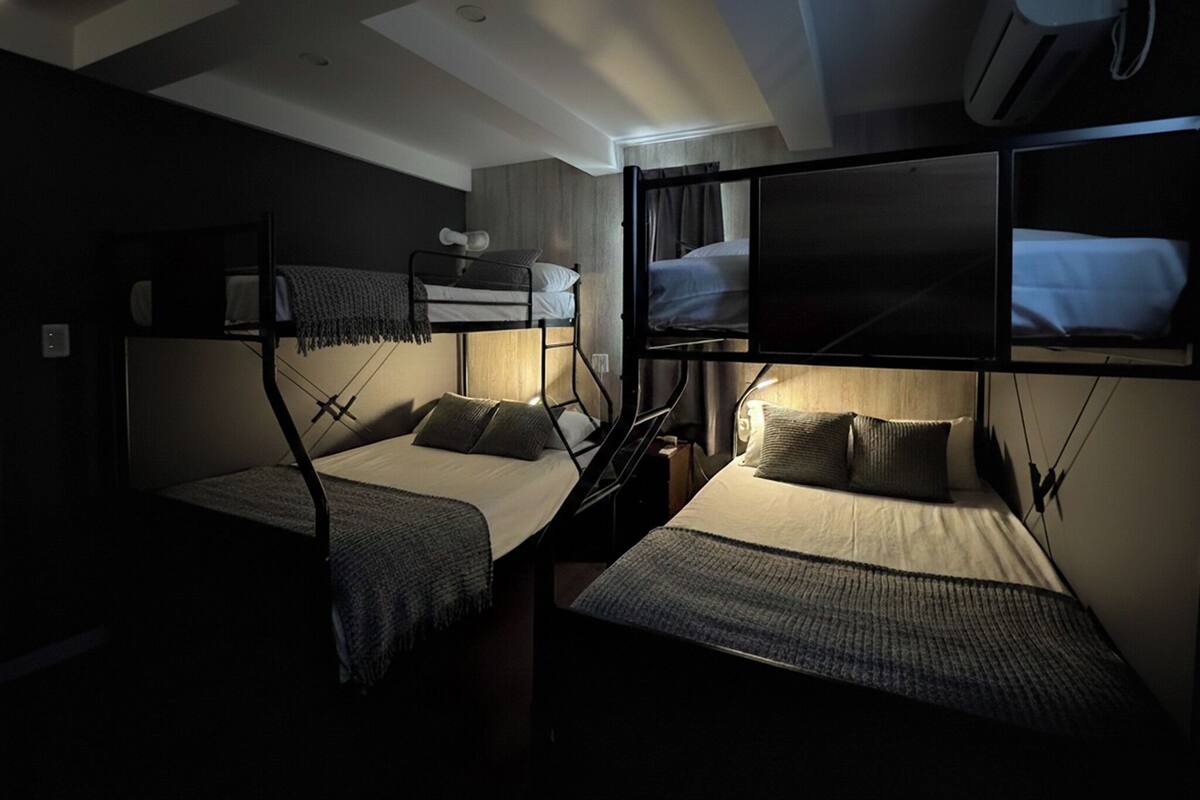 Une chambre de dortoir avec des lits superposés, un téléviseur fixé au mur et un ventilateur de plafond.